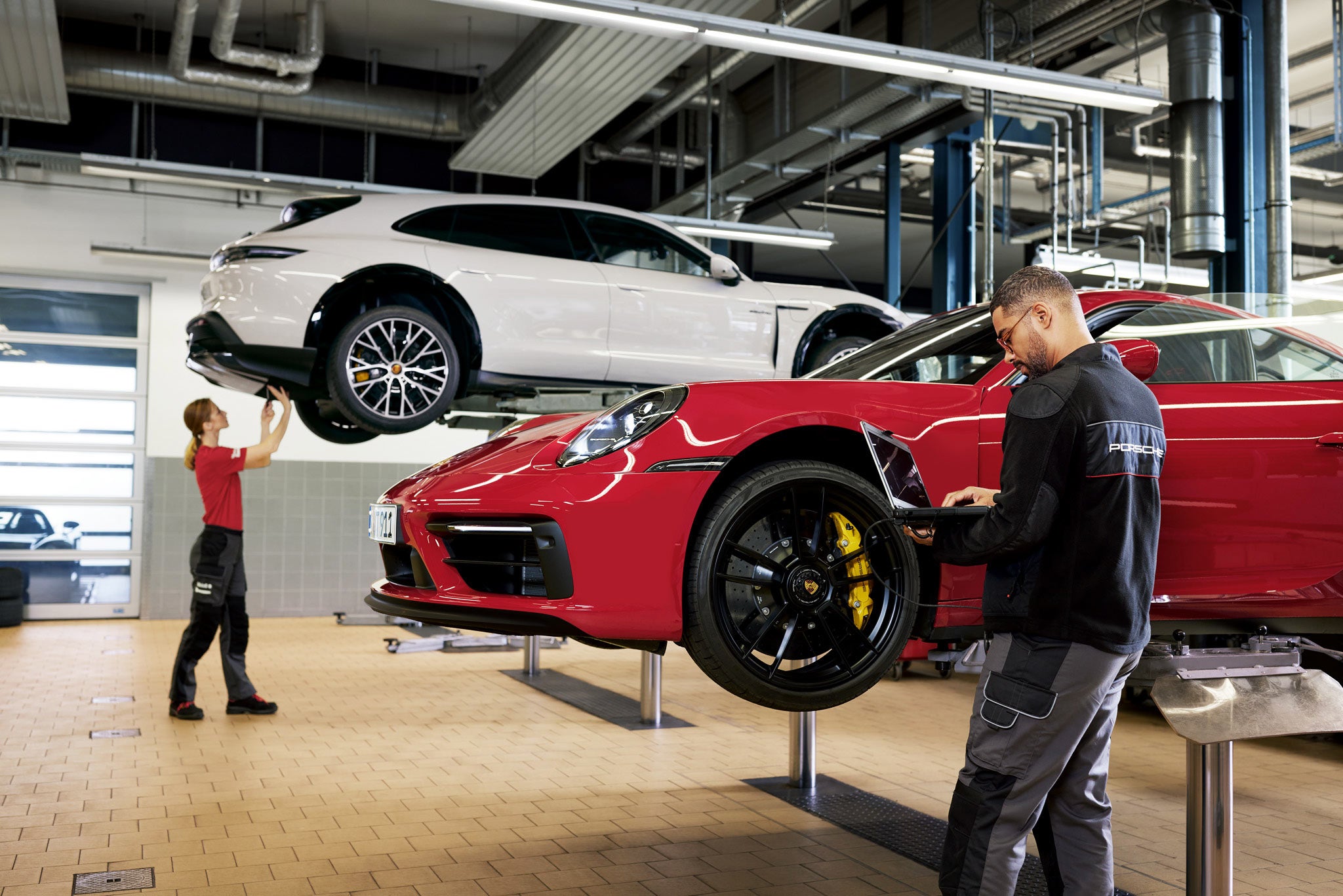 Porsche Certified Service Technicians performing evaluation on a white Porsche Macan and a red Porsche 911