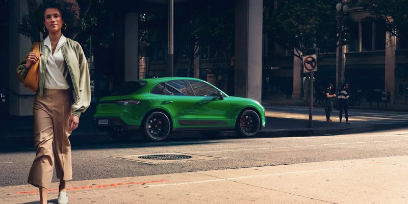 Image of a woman walking away from a green 2024 Porsche Macan parked on a city street