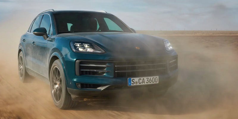 Teal blue 2024 Porsche Cayenne driving on dirt in the desert on a sunny day